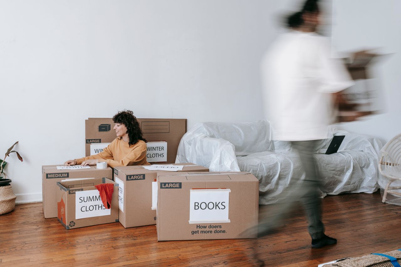 A couple is packing labeled boxes in a clean, minimalist living room as they get ready for moving day.
